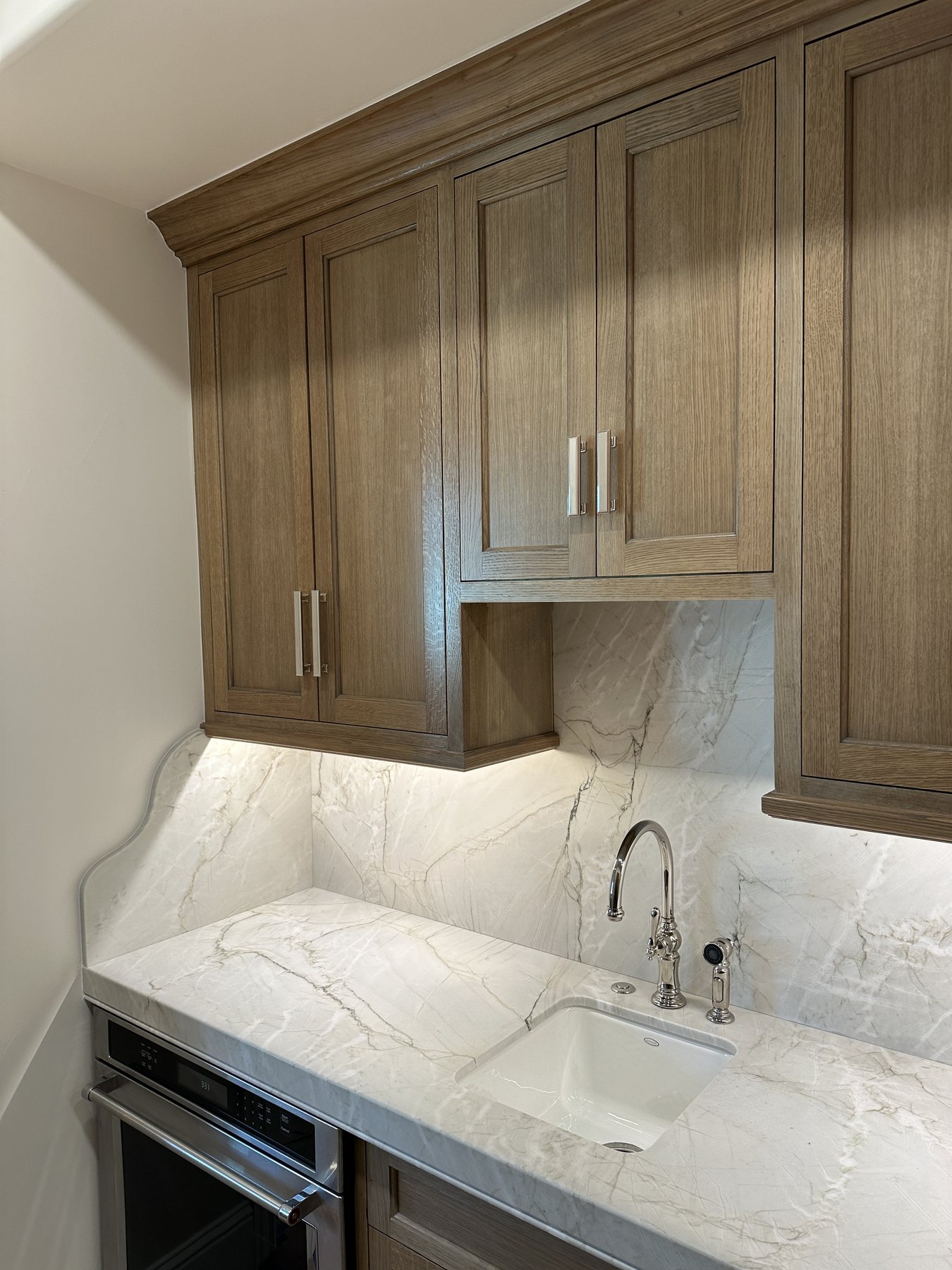 Custom wood cabinetry and full-height stone surface above a utility sink