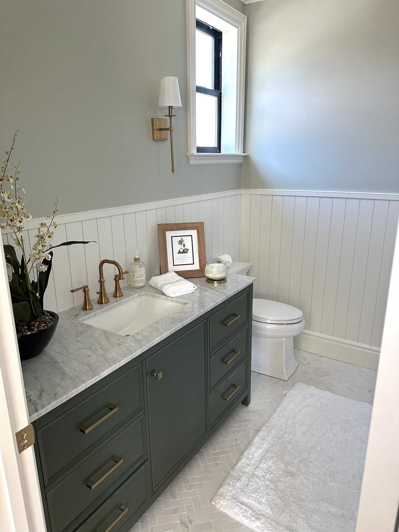 Finished bathroom with green vanity, marble counter, brass fixtures, and paneled walls